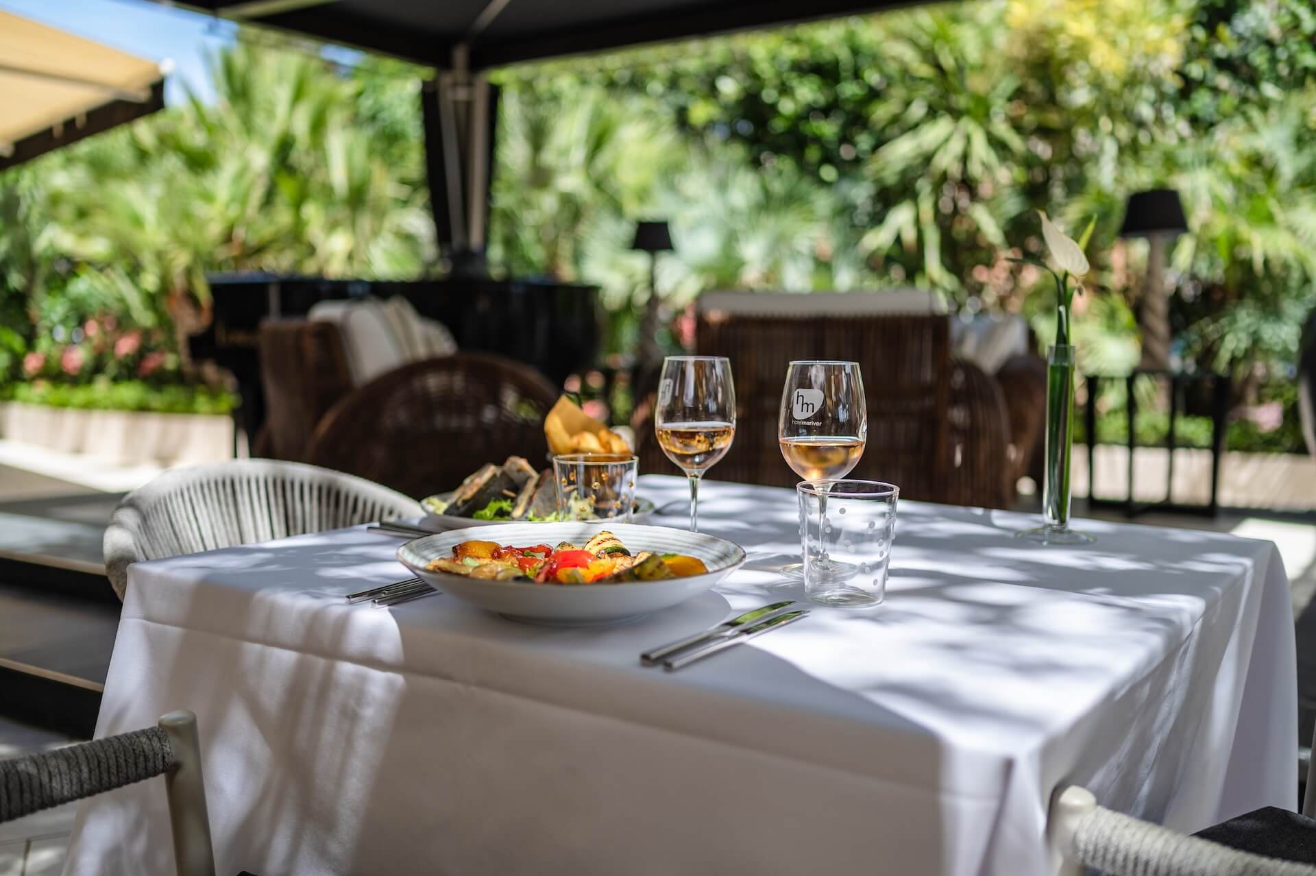 pranzo all'esterno con calici di vino marchiati hotel Mariver e piatti di carne e verdure